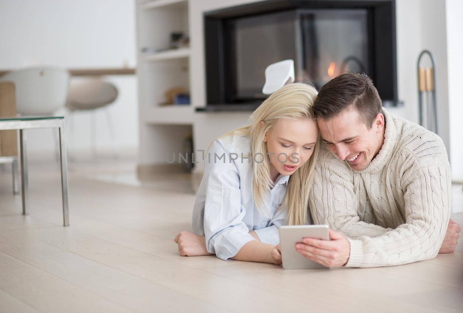 Young Couple on the floor in front of fireplace surfing internet using digital tablet on cold winter day