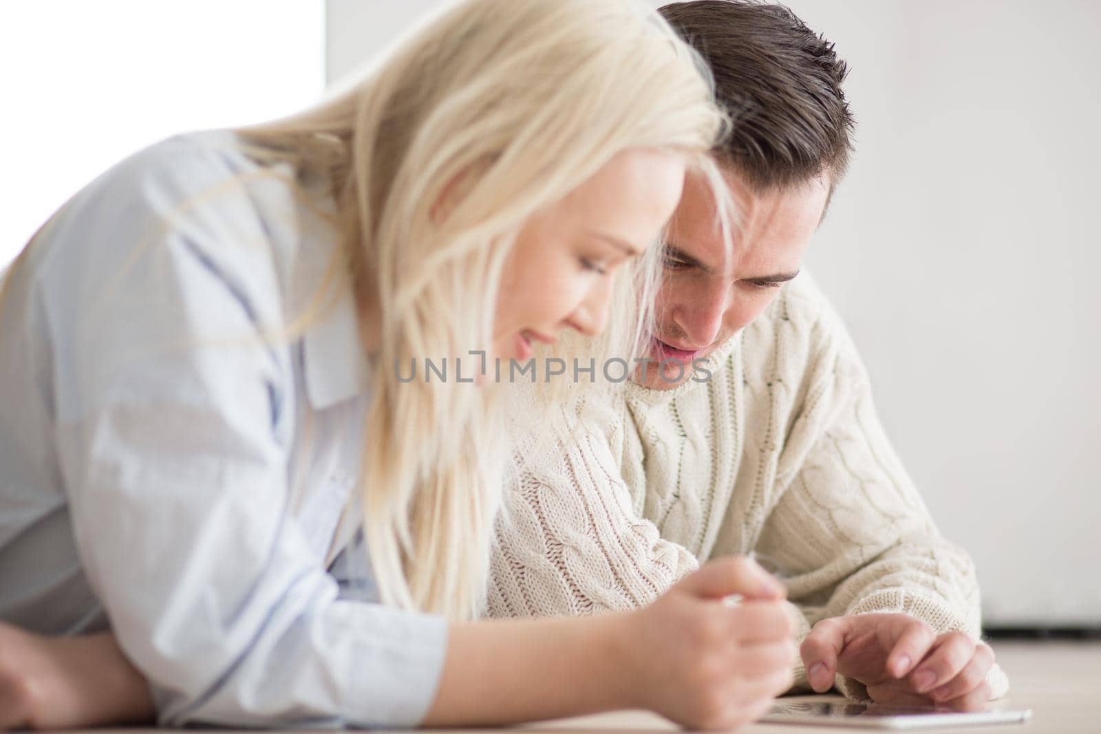 Young Couple on the floor in front of fireplace surfing internet using digital tablet on cold winter day