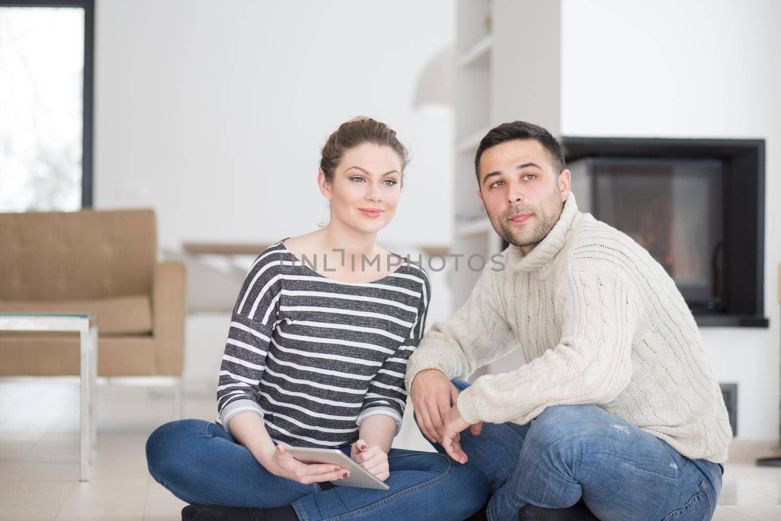 Young Couple on the floor in front of fireplace surfing internet using digital tablet on cold winter day