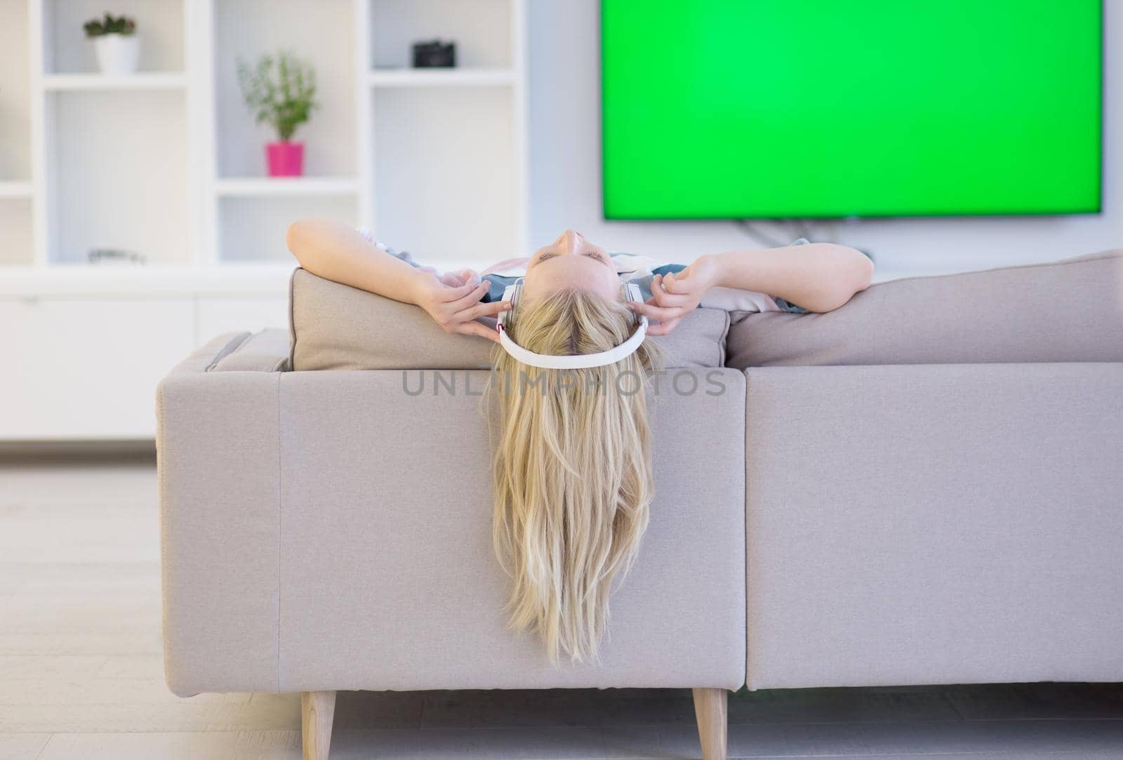 Young beautiful girl enjoying music through headphones, laying on sofa at home