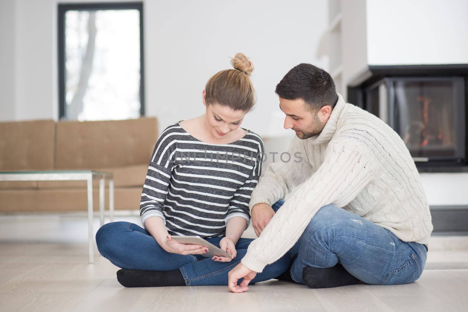 Young Couple on the floor in front of fireplace surfing internet using digital tablet on cold winter day