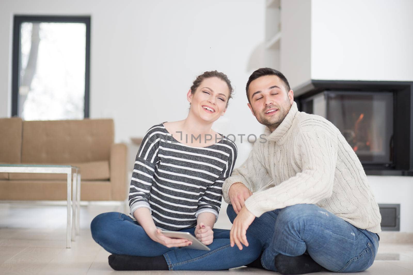 Young Couple on the floor in front of fireplace surfing internet using digital tablet on cold winter day