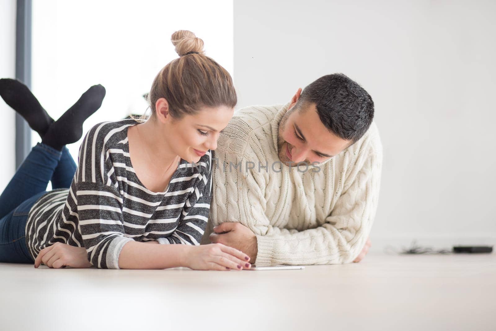 Young Couple on the floor in front of fireplace surfing internet using digital tablet on cold winter day