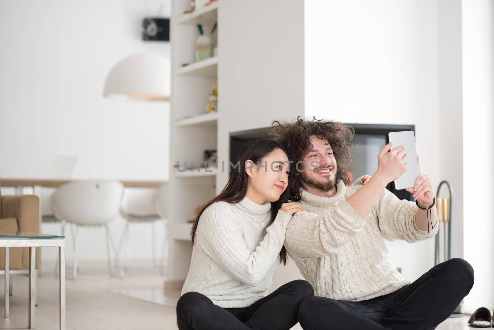 beautiful young multiethnic couple using tablet computer in front of fireplace on cold winter day at home