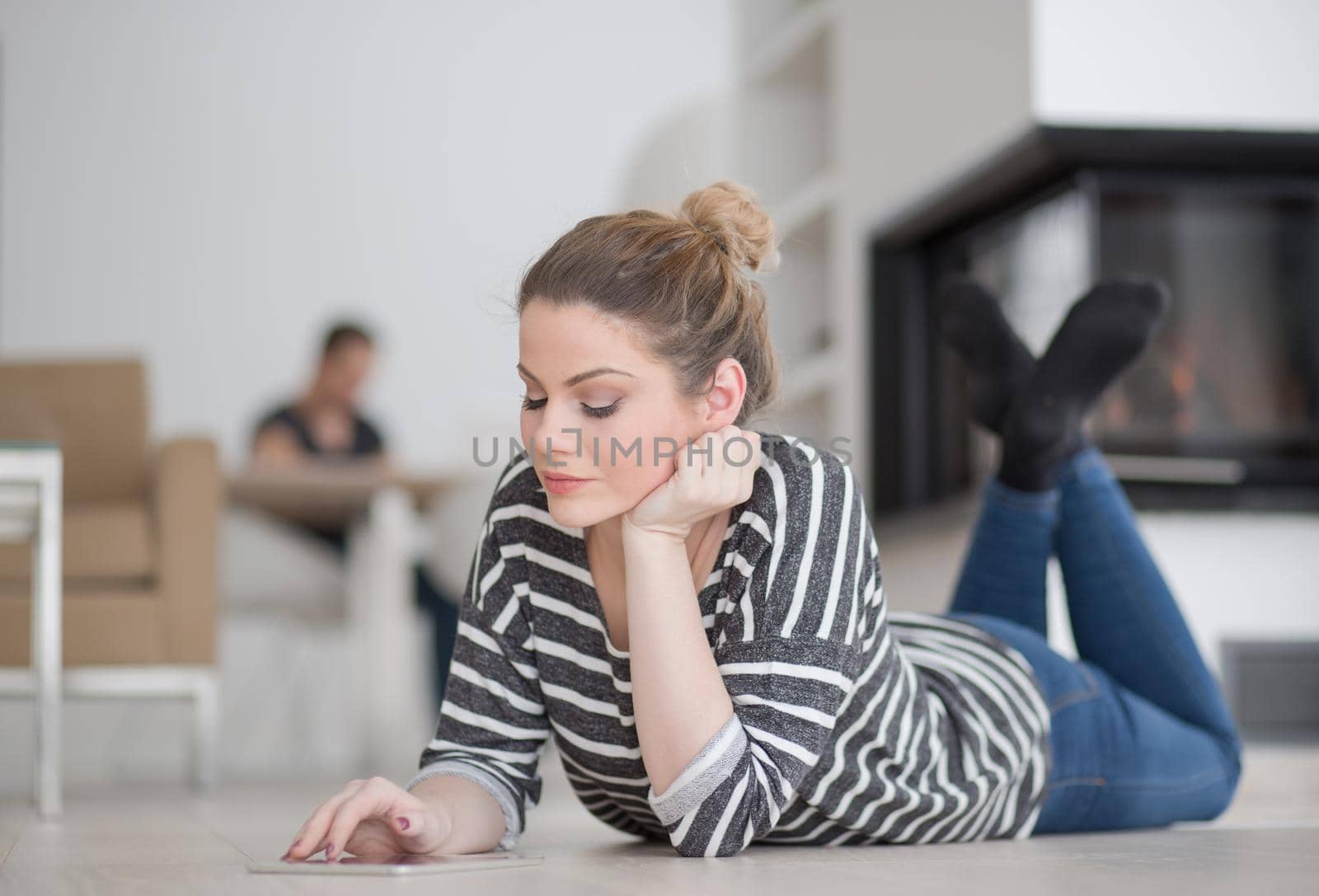 beautiful young woman websurfing using tablet computer on the floor in front of fireplace on cold winter day at home