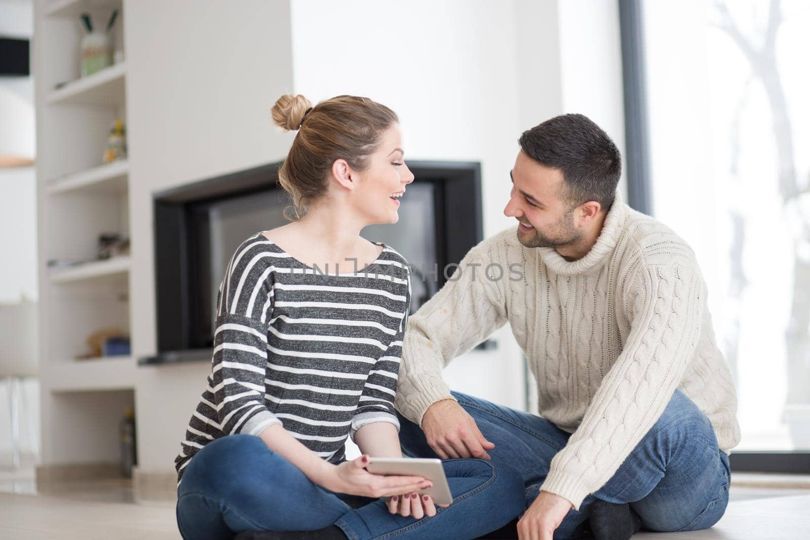 Young Couple on the floor in front of fireplace surfing internet using digital tablet on cold winter day