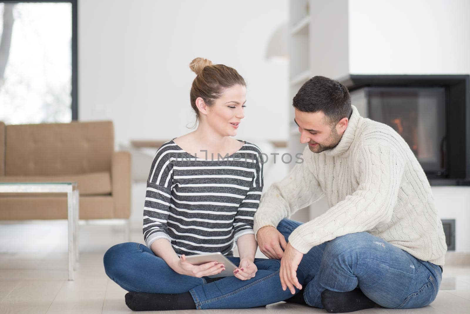 Young Couple on the floor in front of fireplace surfing internet using digital tablet on cold winter day