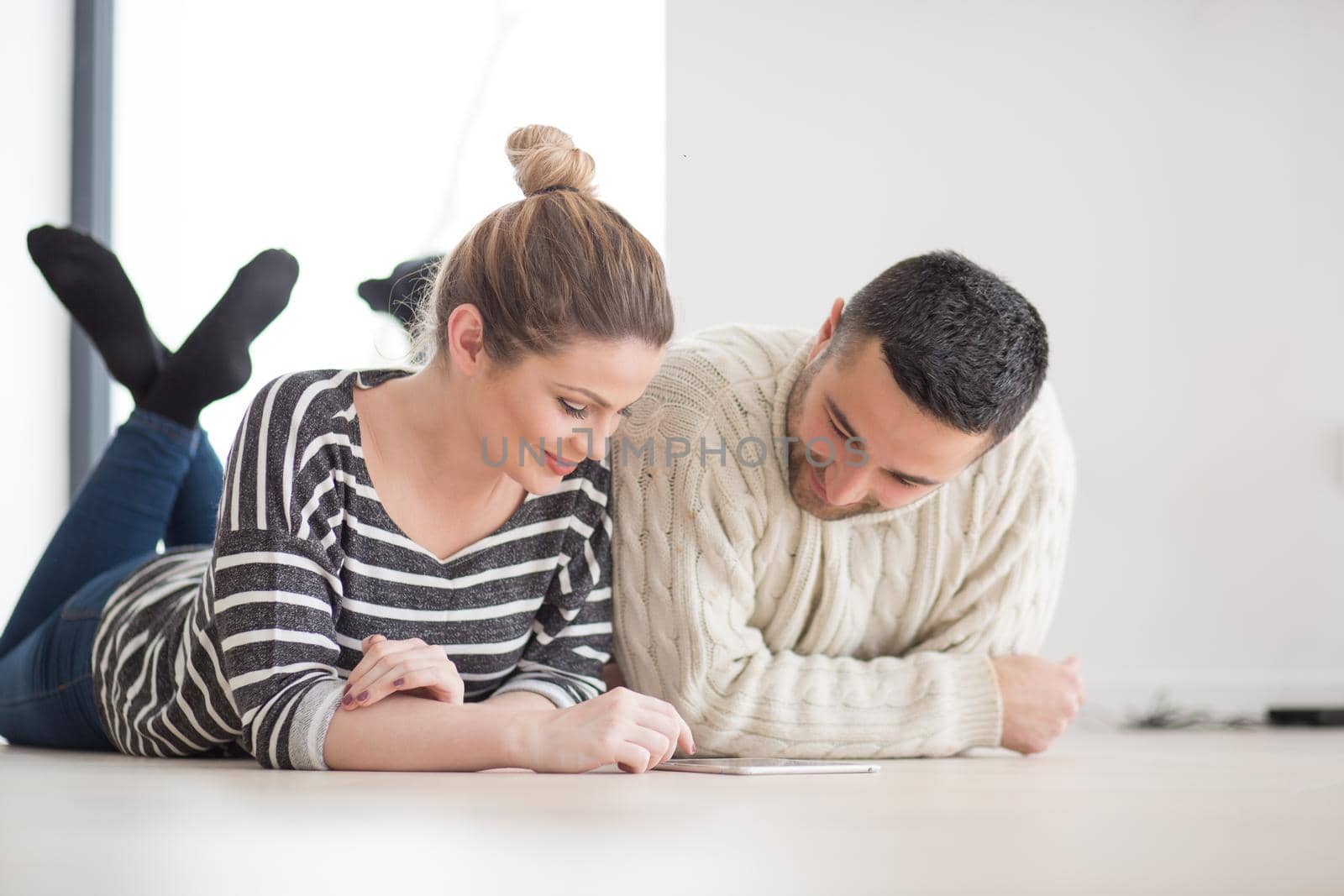 Young Couple on the floor in front of fireplace surfing internet using digital tablet on cold winter day