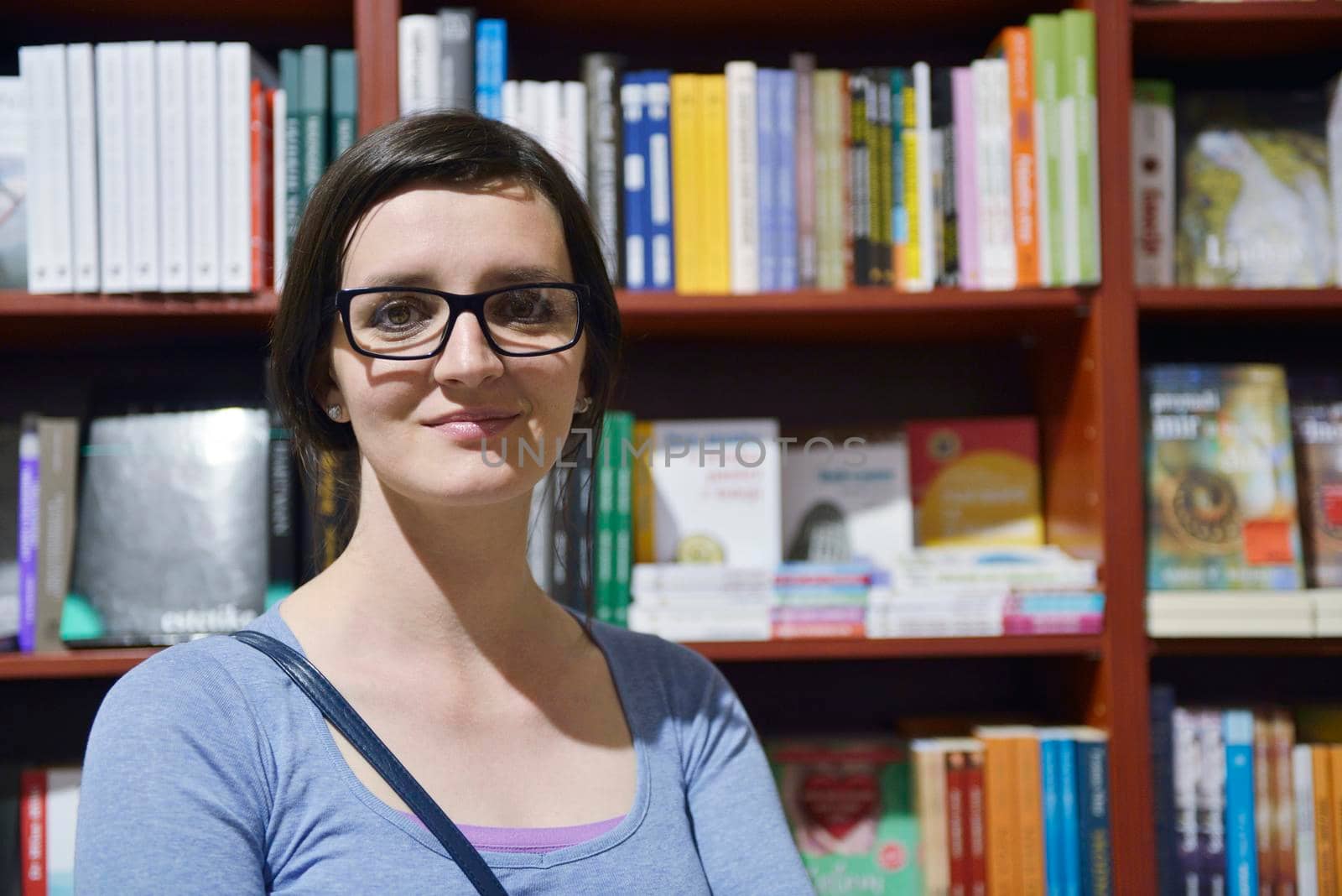 Pretty female student standing at bookshelf in university library store shop  searching for a book