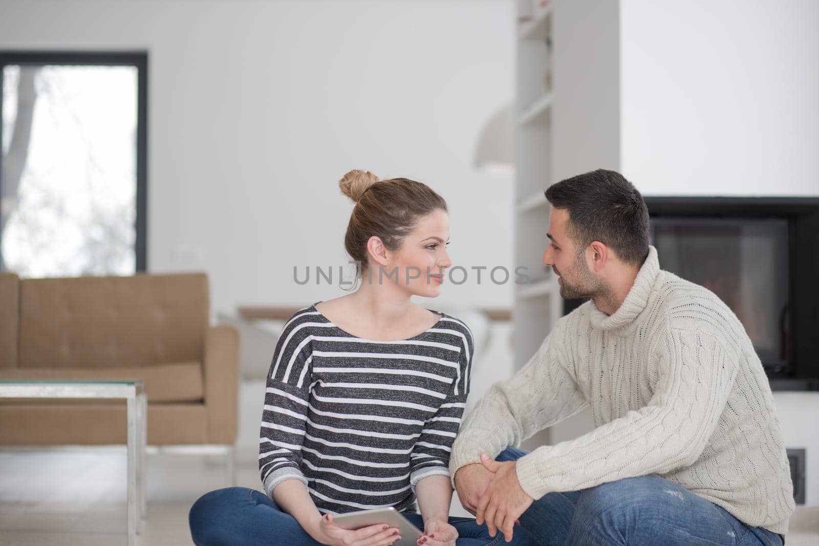 Young Couple on the floor in front of fireplace surfing internet using digital tablet on cold winter day