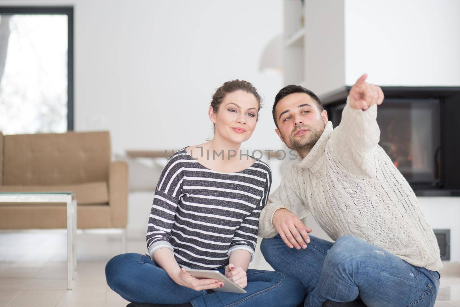 Young Couple on the floor in front of fireplace surfing internet using digital tablet on cold winter day