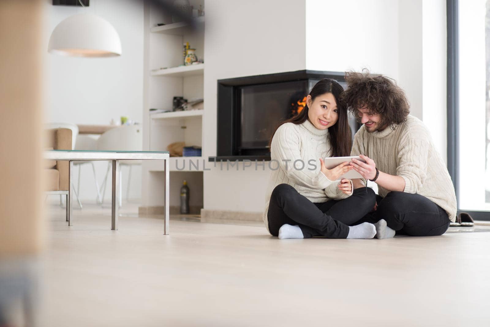 multiethnic couple using tablet computer in front of fireplace by dotshock