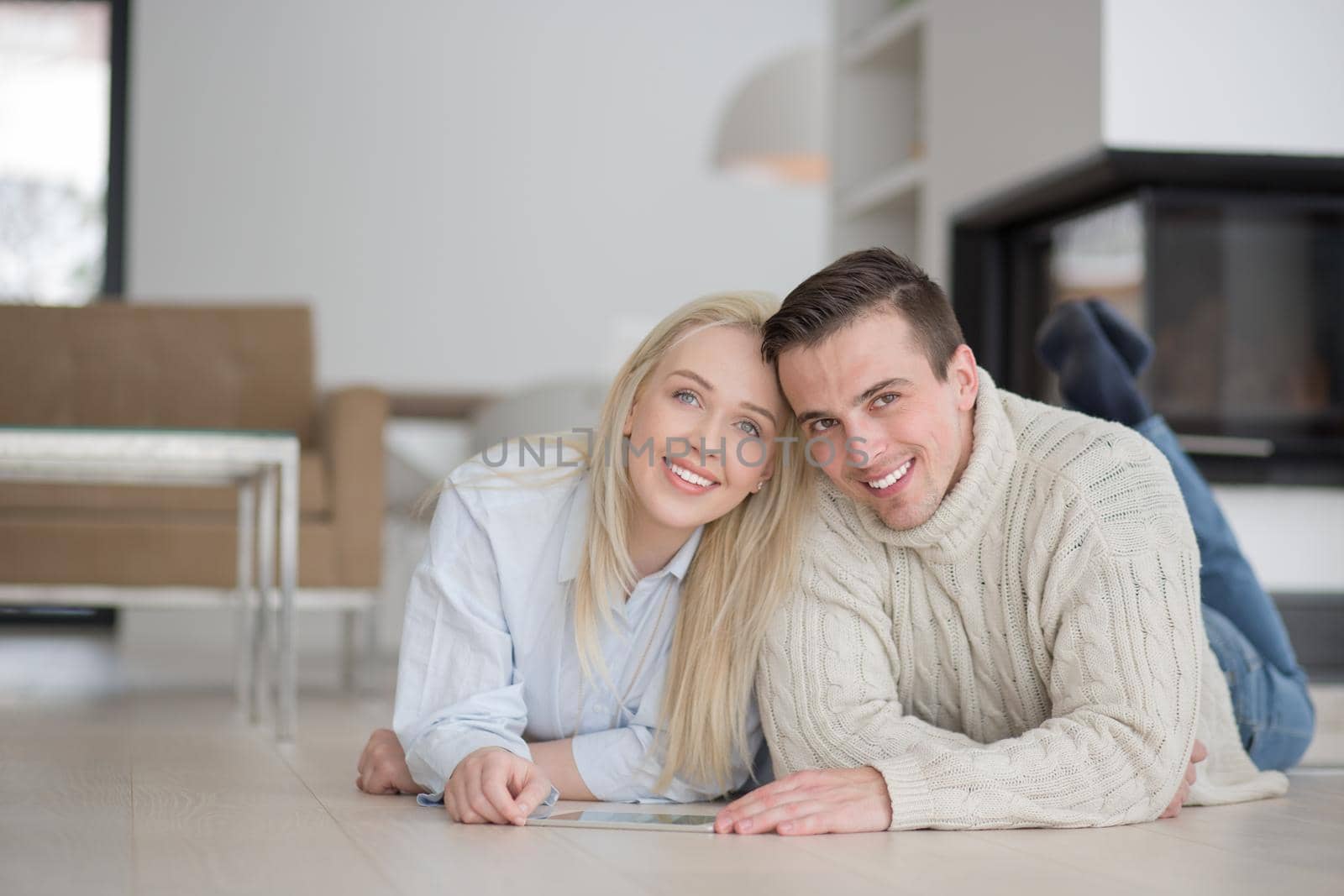 Young Couple on the floor in front of fireplace surfing internet using digital tablet on cold winter day