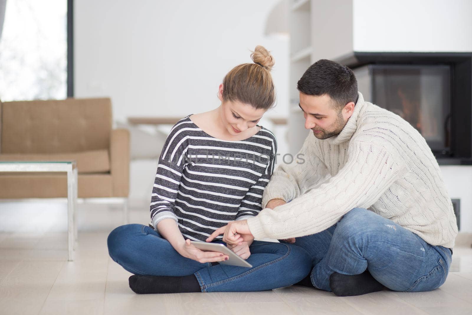 Young Couple on the floor in front of fireplace surfing internet using digital tablet on cold winter day