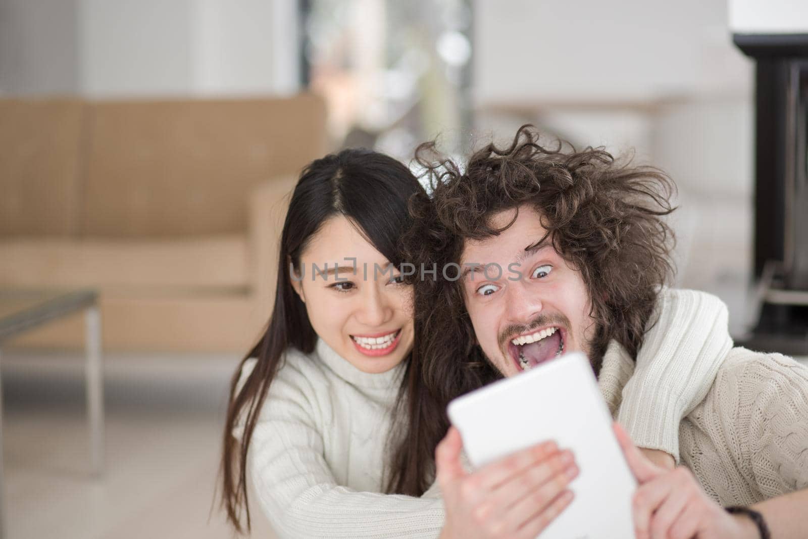 beautiful young multiethnic couple using tablet computer in front of fireplace on cold winter day at home