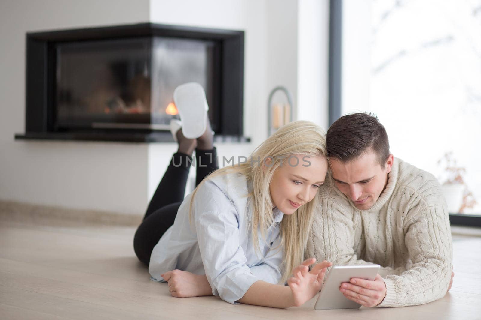 Young Couple on the floor in front of fireplace surfing internet using digital tablet on cold winter day