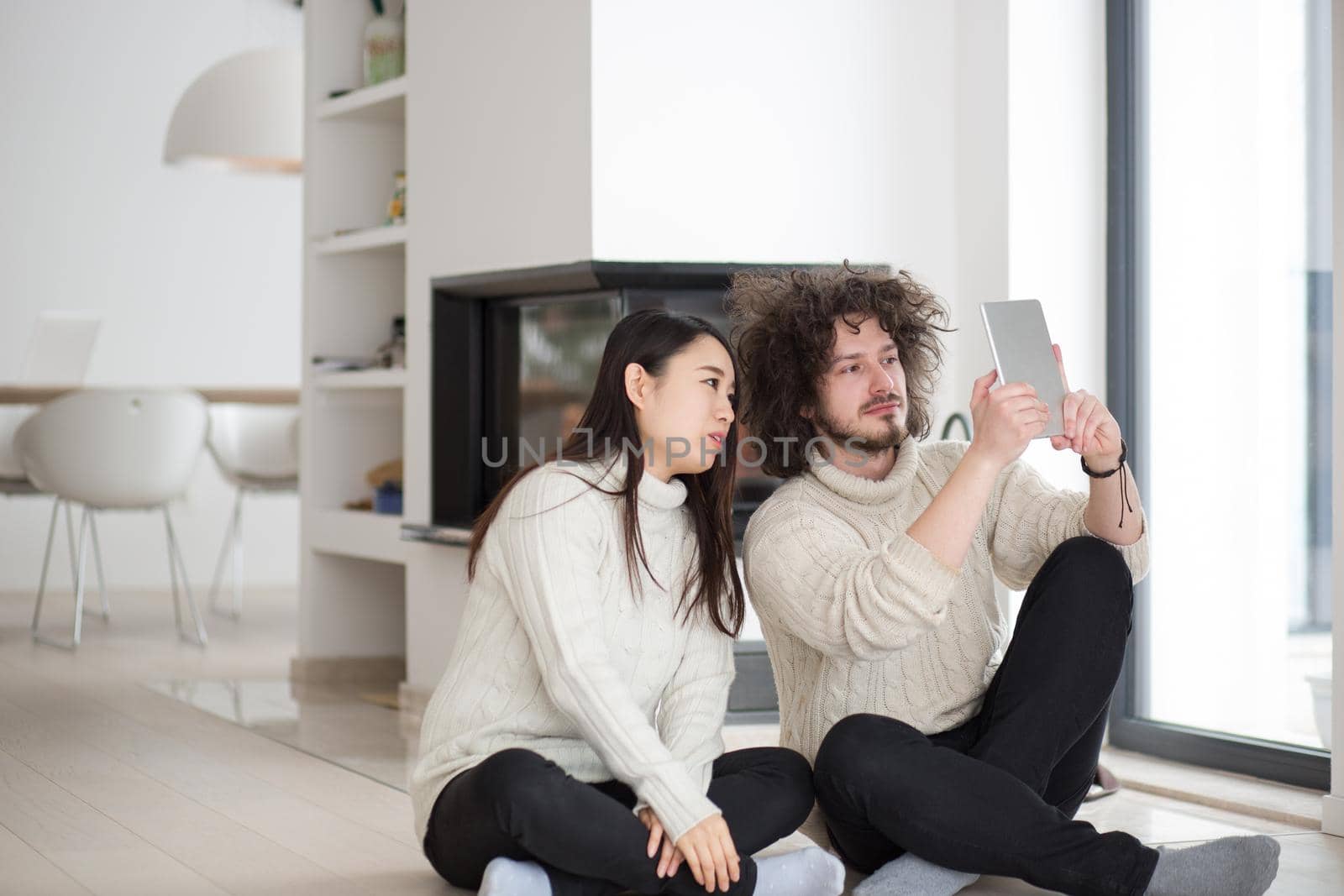 beautiful young multiethnic couple using tablet computer in front of fireplace on cold winter day at home