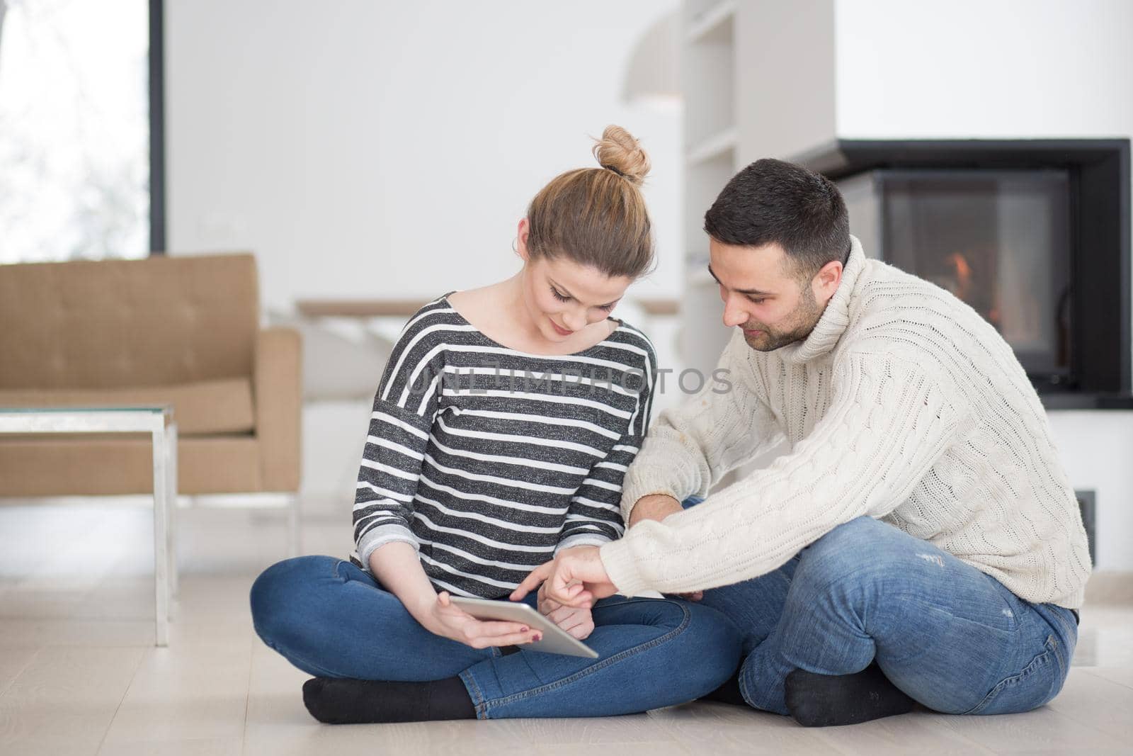 Young Couple on the floor in front of fireplace surfing internet using digital tablet on cold winter day