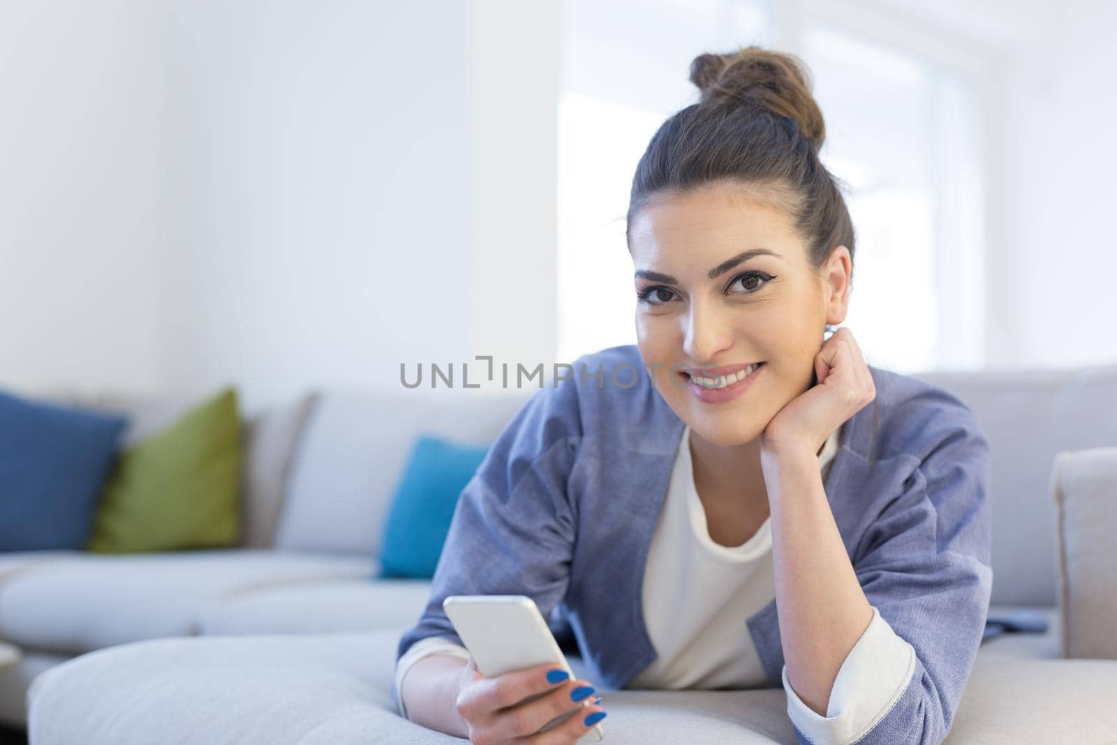 young happy woman using mobile phone on sofa at luxury home