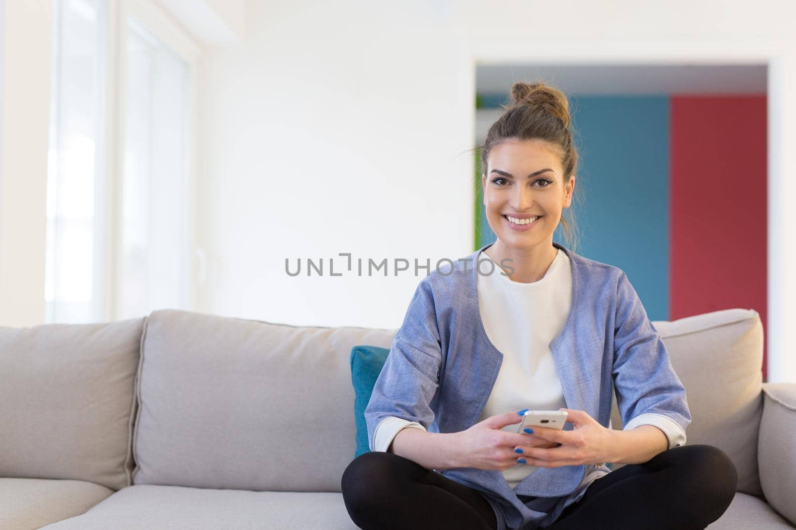 young happy woman using mobile phone on sofa at luxury home