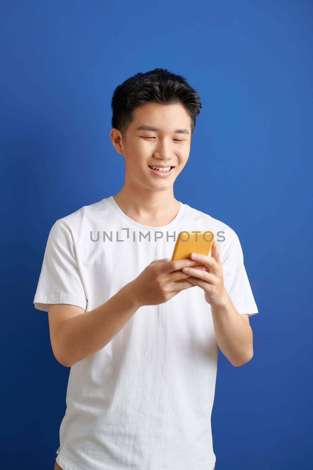 Smiling young good looking Asian man using smartphone to get in touch with family and friends isolated on blue  background