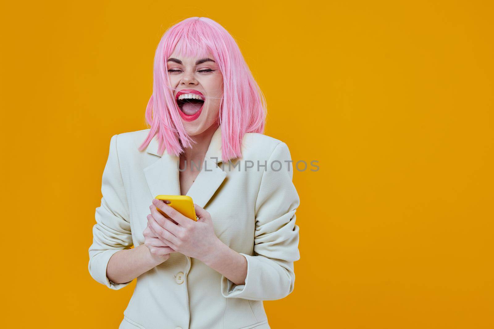 cheerful woman with pink hair with a phone in a white suit yellow background. High quality photo