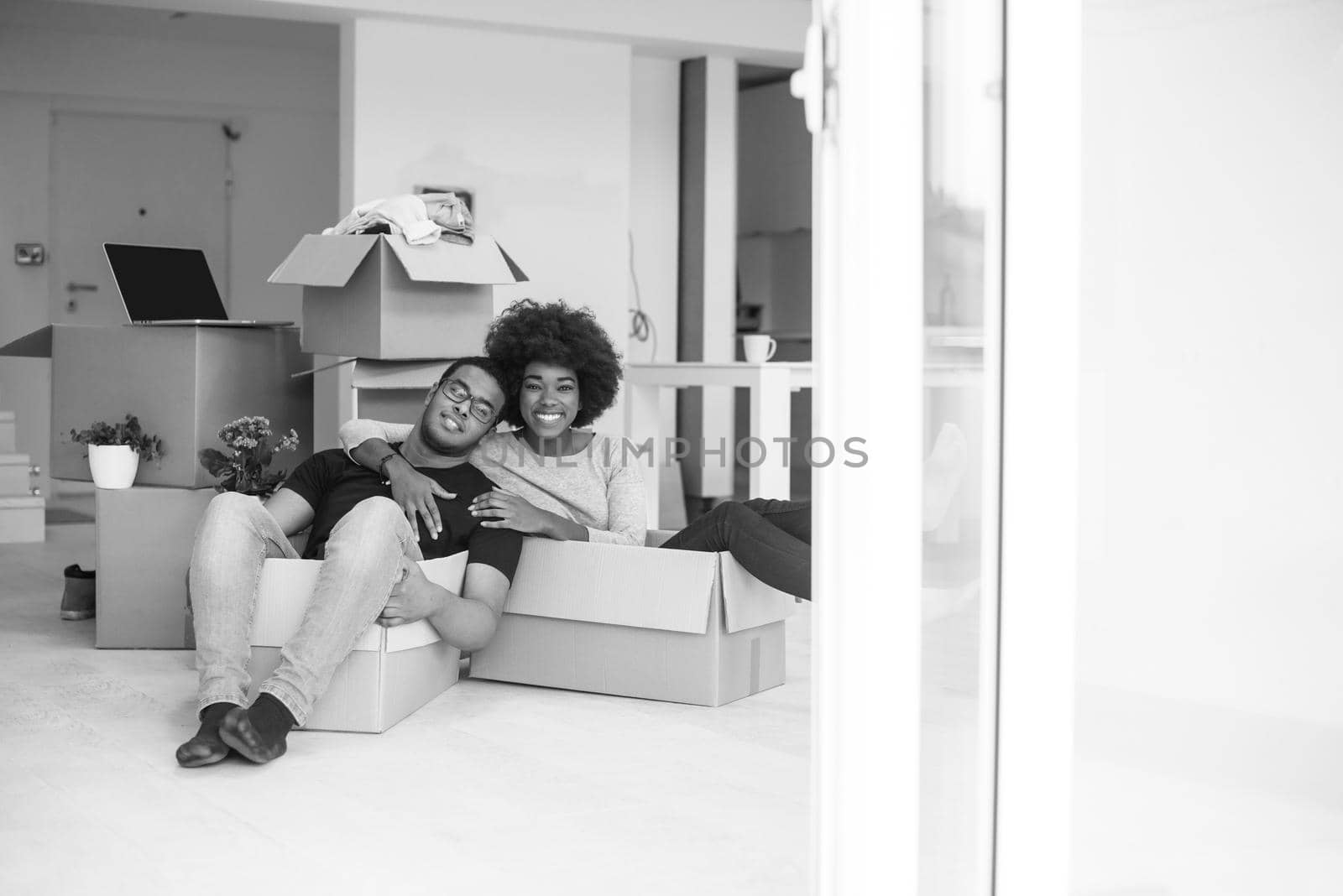 African American couple sitting in a box playing with packing material, having fun after moving in new home