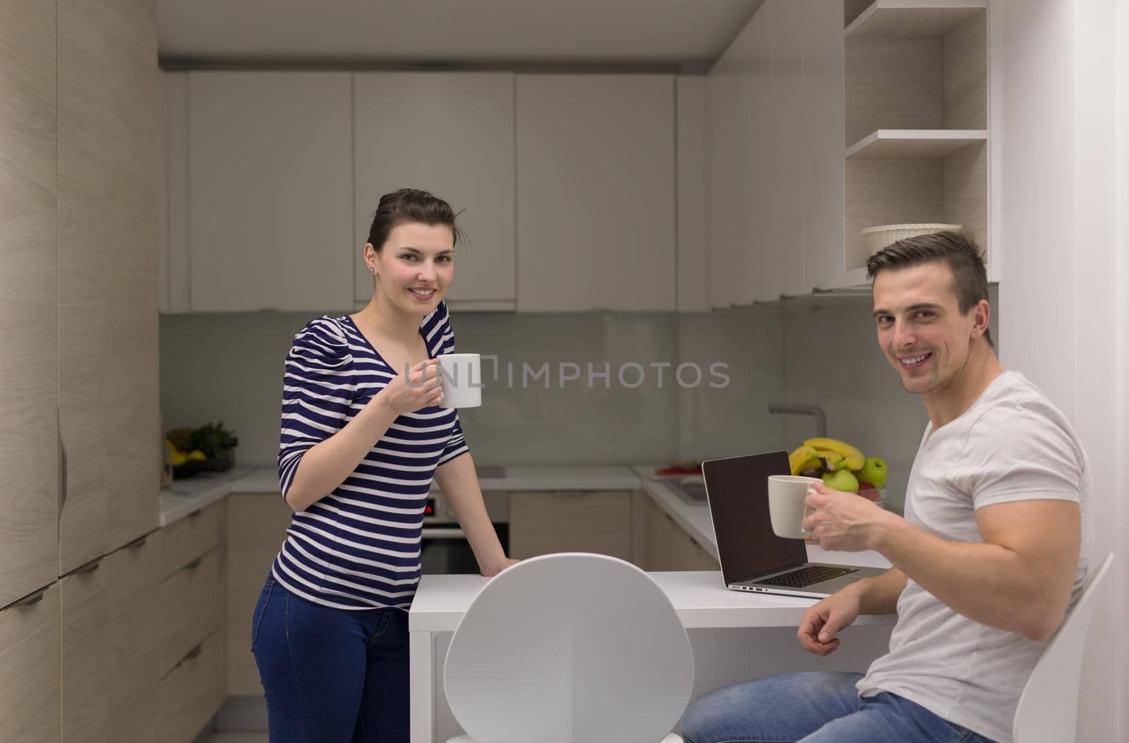 happy young couple with laptop computer enjoying morning coffee in modern kitchen at home