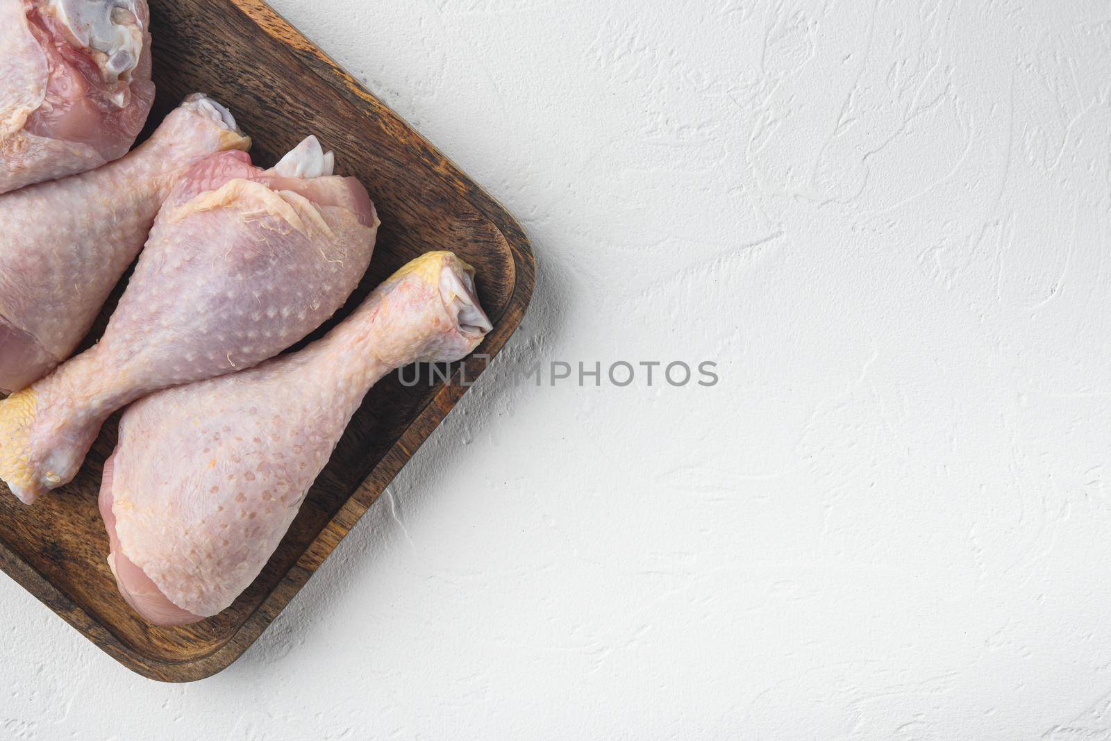 Uncooked Chicken Thigh or legs, drumsticks set, on wooden tray, on white stone background, top view flat lay, with copy space for text