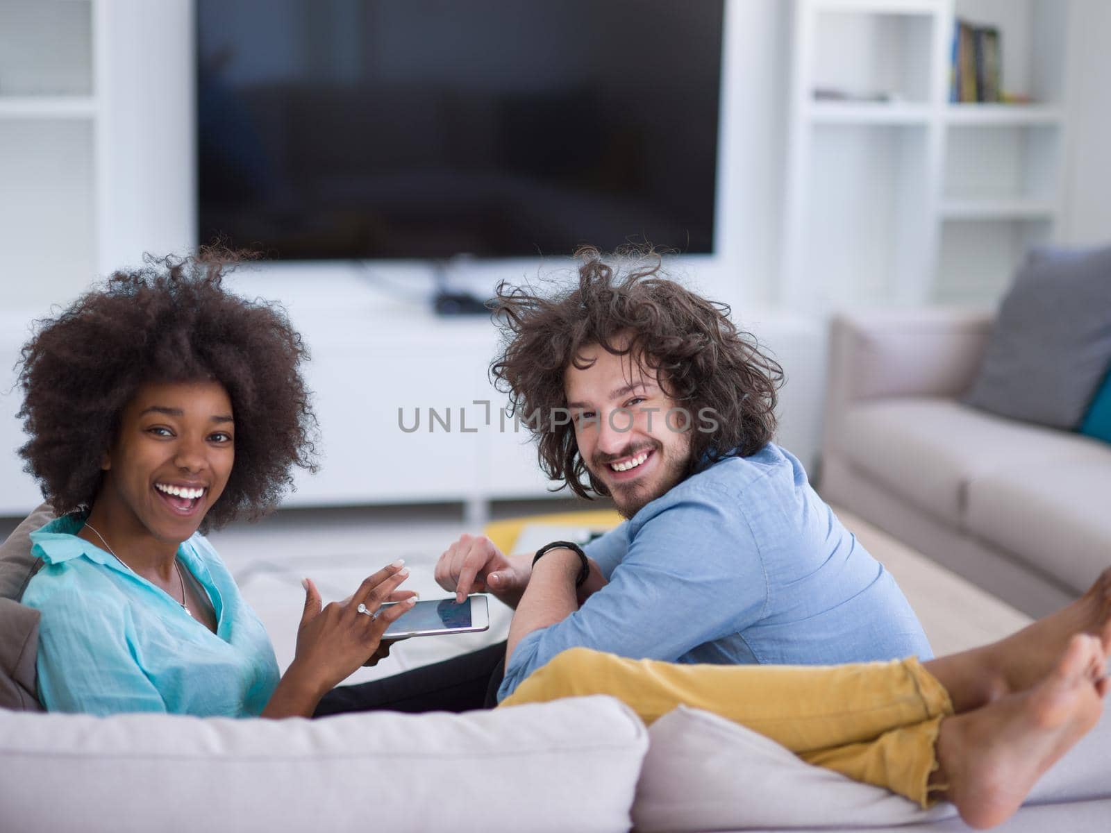 Young multiethnic couple sitting on a sofa in the luxury living room, using a tablet computer