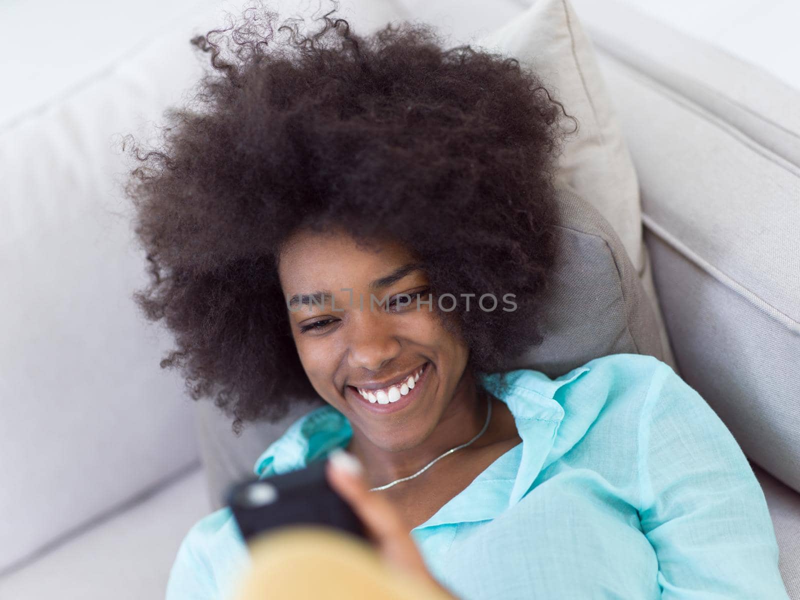 black woman sitting on sofa and using mobile phone by dotshock