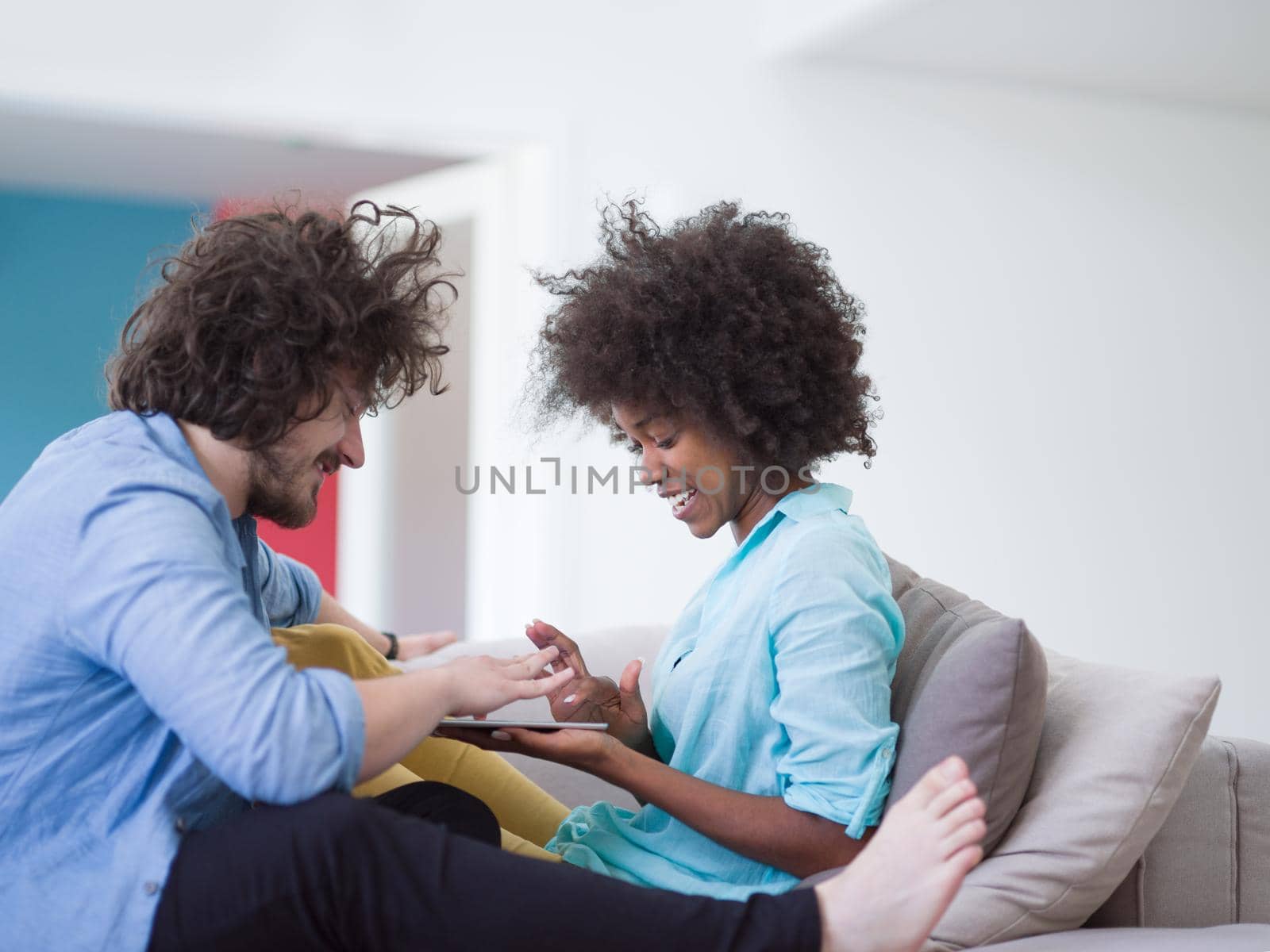 Young multiethnic couple sitting on a sofa in the luxury living room, using a tablet computer