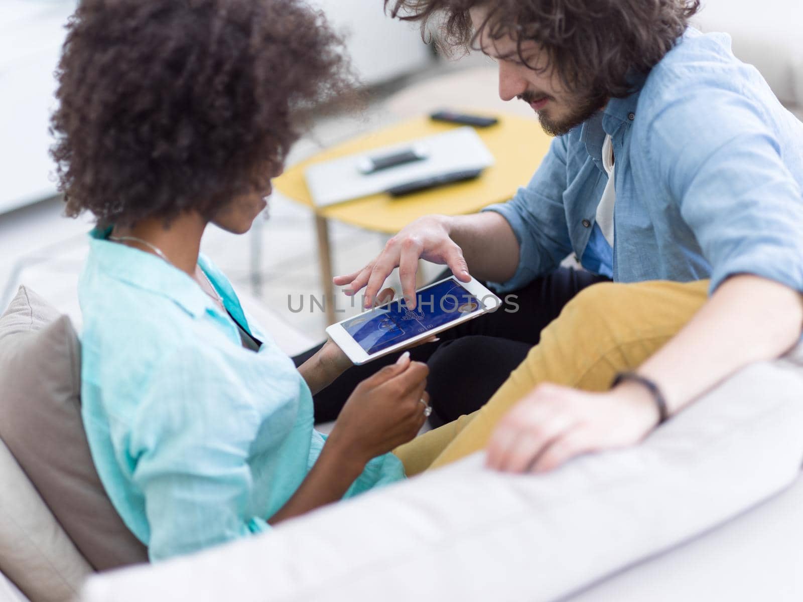 Young multiethnic couple sitting on a sofa in the luxury living room, using a tablet computer