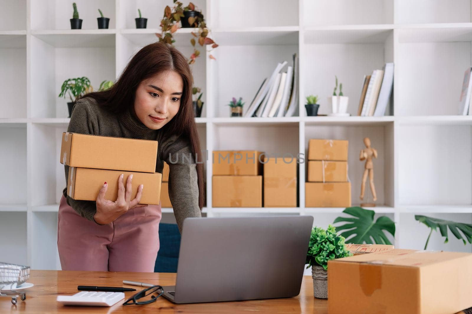 Start up small business entrepreneur SME or freelance asian woman using laptop with box, Young success Asian woman with her hand lift up , online marketing packaging box and delivery, SME concept. by nateemee