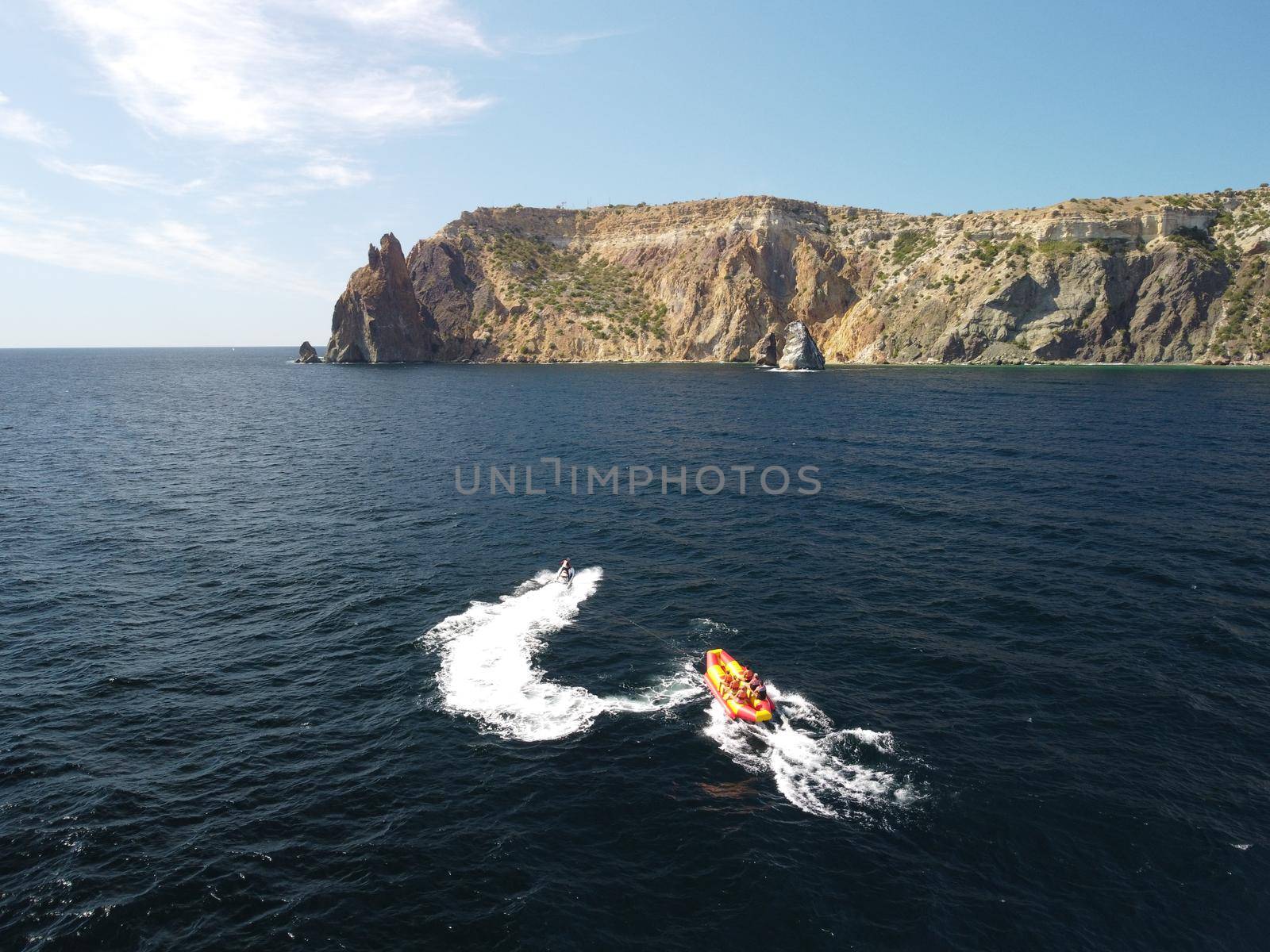 Happy people swim on air mattress behind a high speed water bike. Tourists ride on inflatable watercraft boat. Sea attraction. Water boat skating people on large Inflatable raft. Aerial copter view