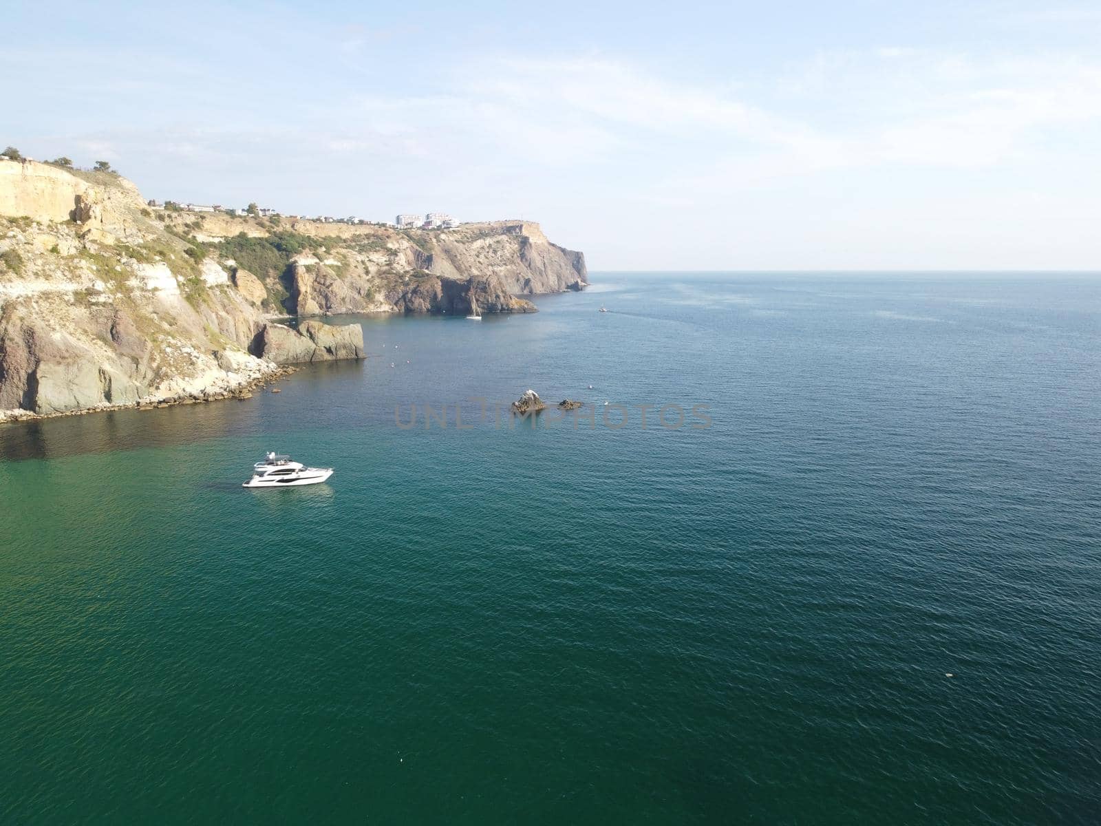 Sea landscape with rocky coastline on sunset time with cloudy sky. Yachts in the Sea on a background of rocky shores. The concept of perfect place for summer travel and rest.