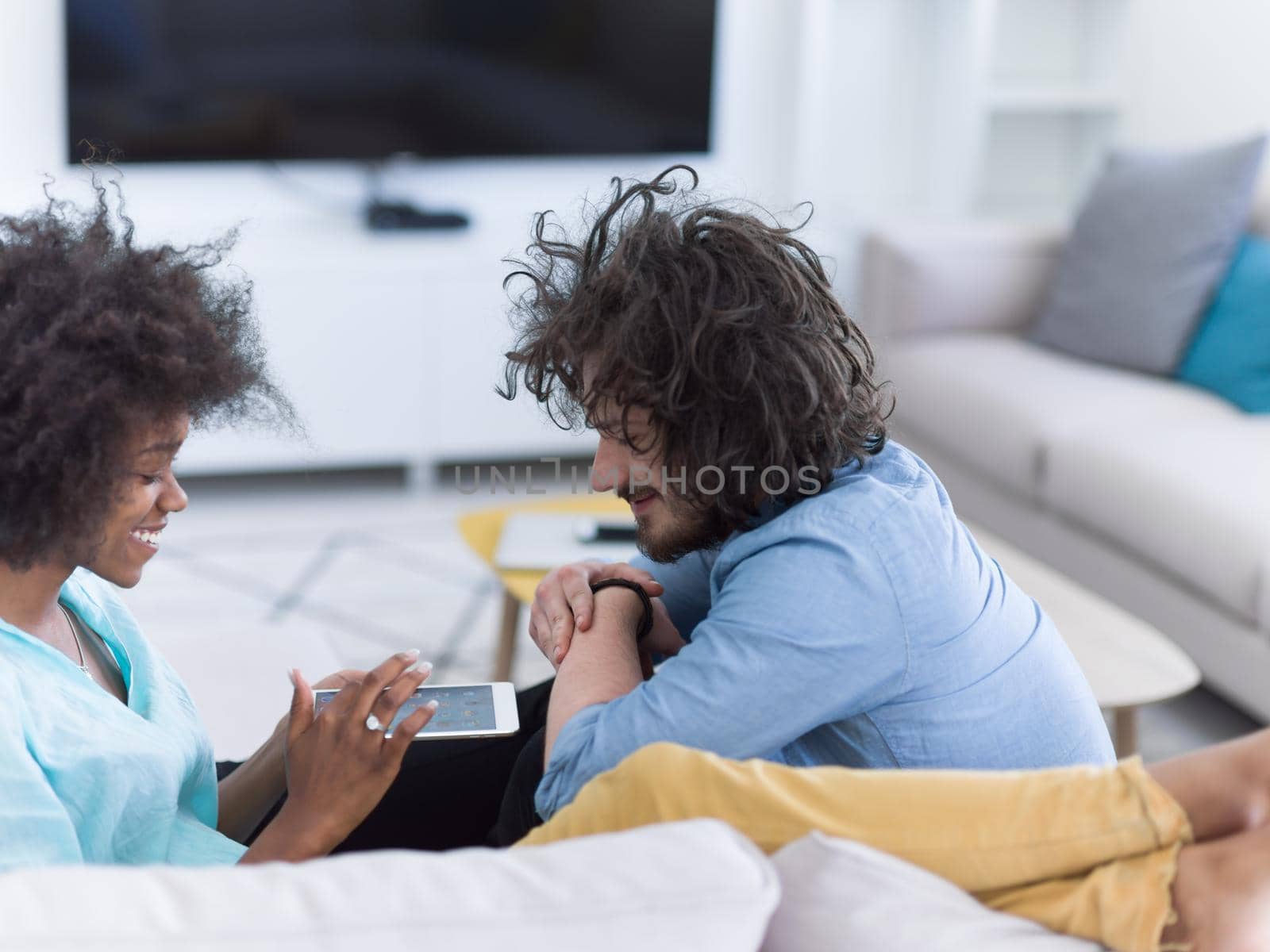 Young multiethnic couple sitting on a sofa in the luxury living room, using a tablet computer