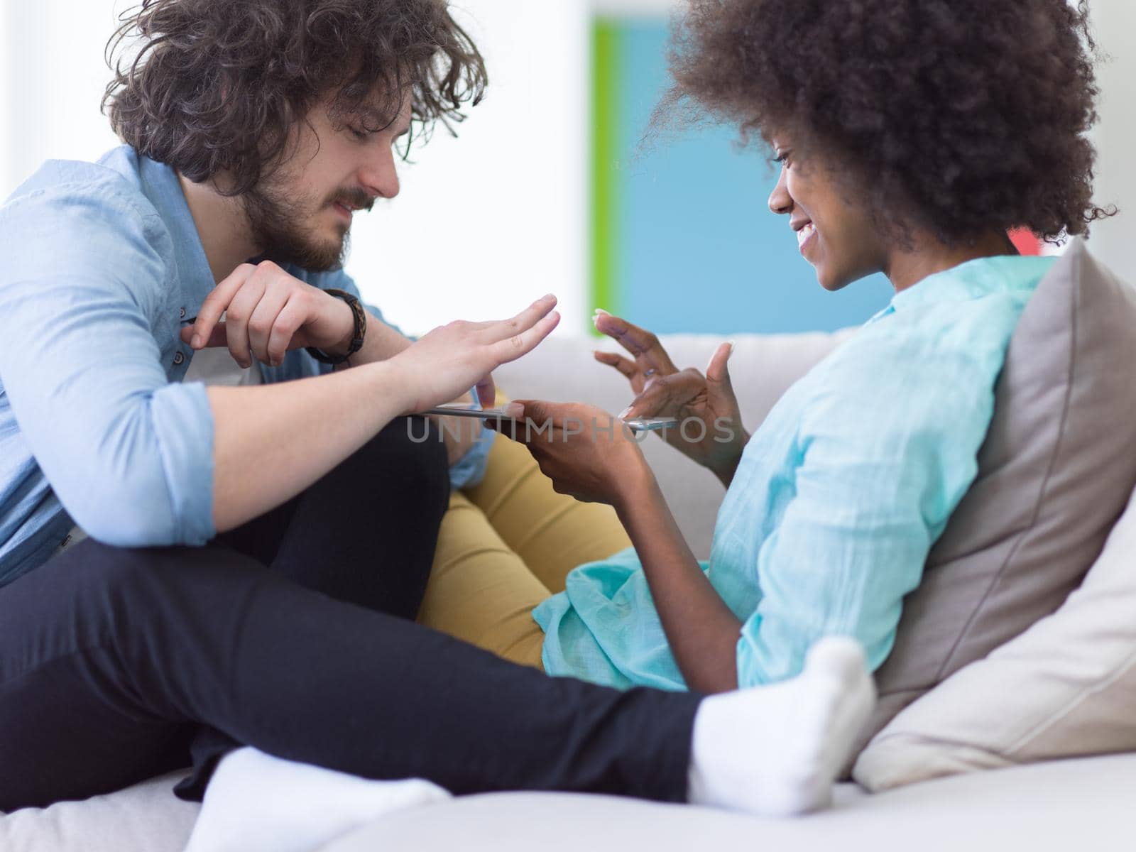 Young multiethnic couple sitting on a sofa in the luxury living room, using a tablet computer