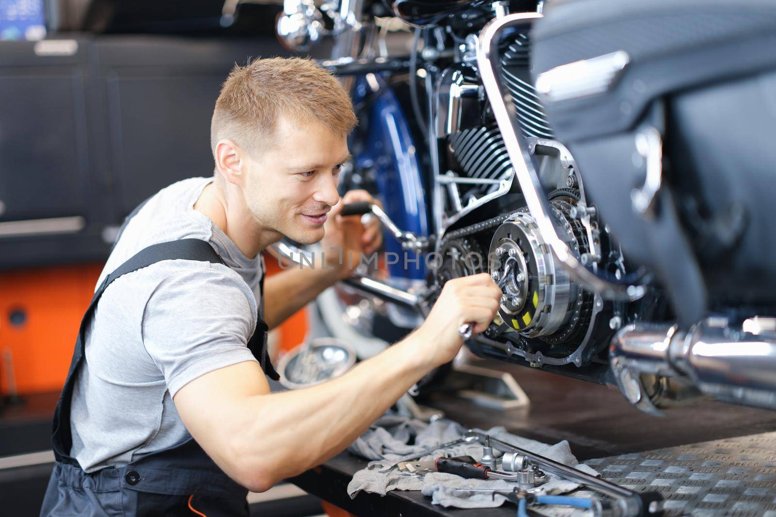 Young male locksmith disassembles motorcycle engine on bench in garage. Motorcycle engine repair concept