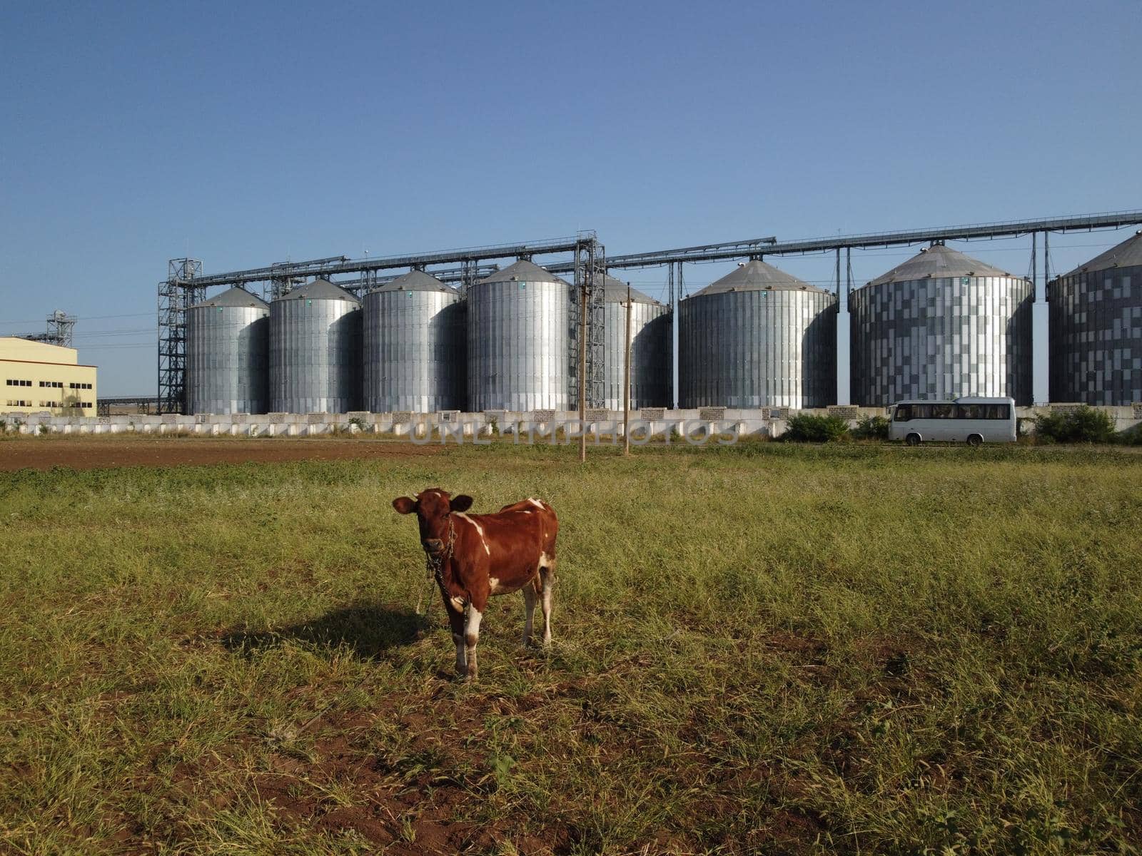 Grain elevator. Metal grain elevator in agricultural zone. Agriculture storage for harvest. Grain elevators on green nature background. Exterior of agricultural factory