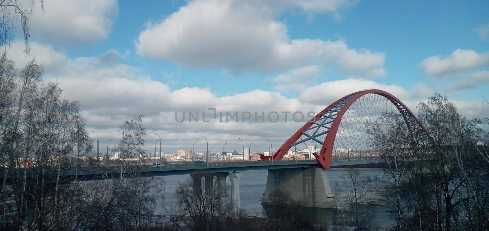 Red arch of the cable-stayed suspension bridge over the wide Ob River. Novosibirsk, Russia. Red suspension bridge over the Ob River. Bugrinsky bridge over the Ob River.