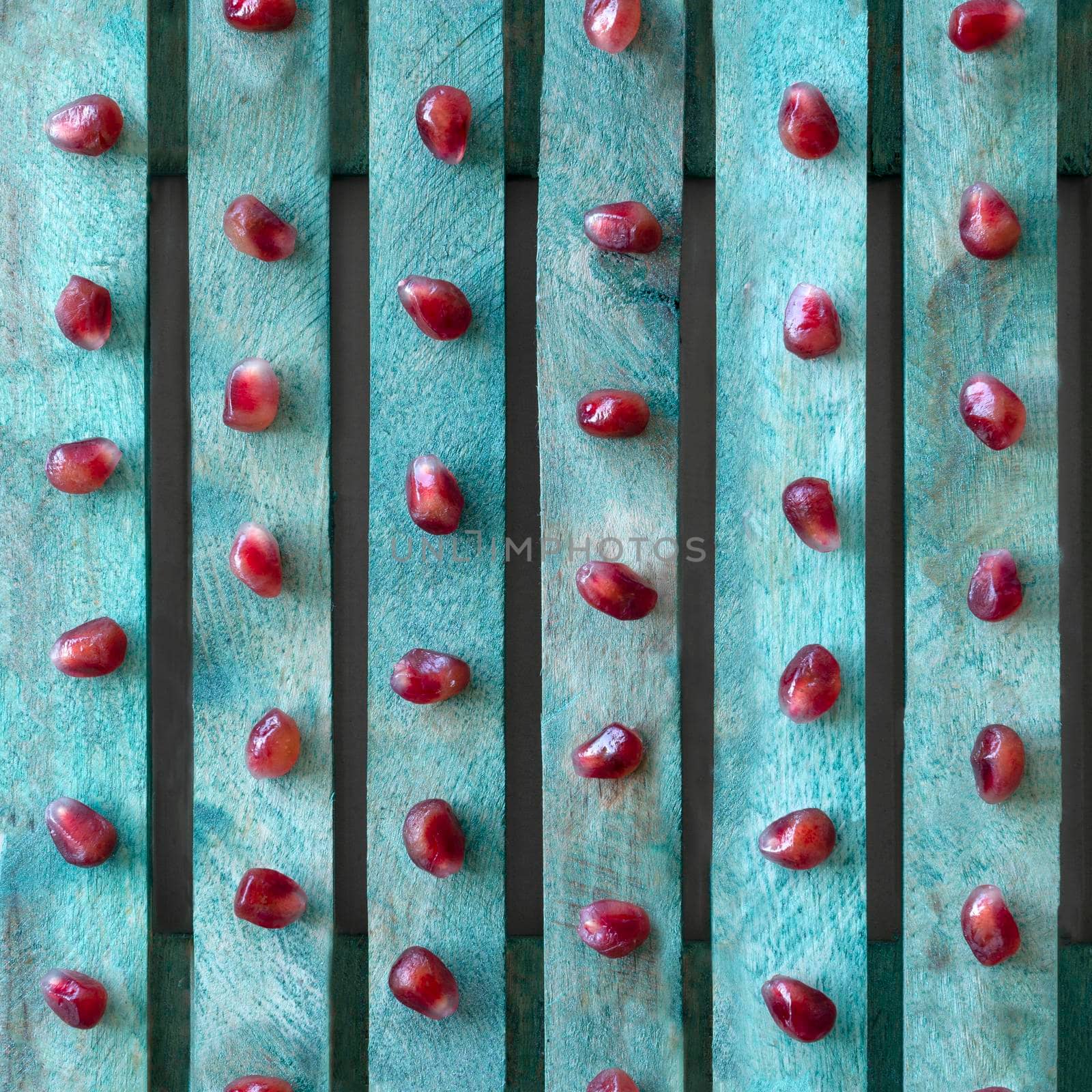 Seamless textured background in contrasting colors. Red pomegranate seeds on a turquoise board.