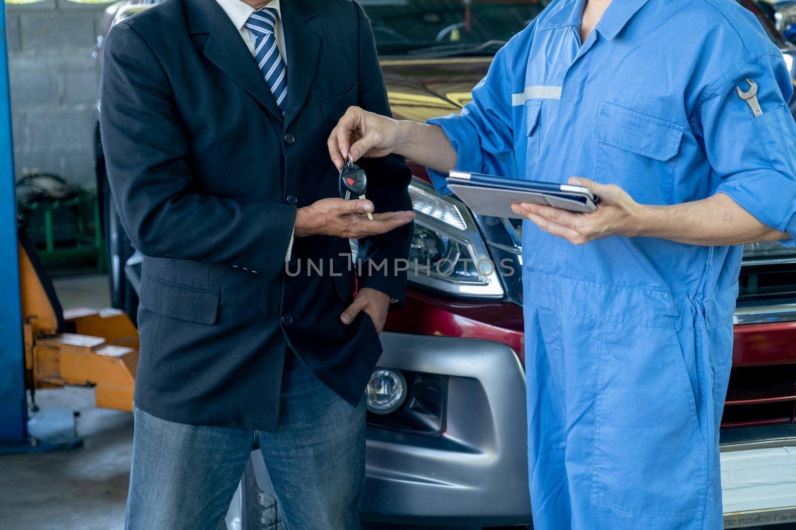 Close up shot automotive technician give car key back to customer after finish fix the problem of car in workplace area.