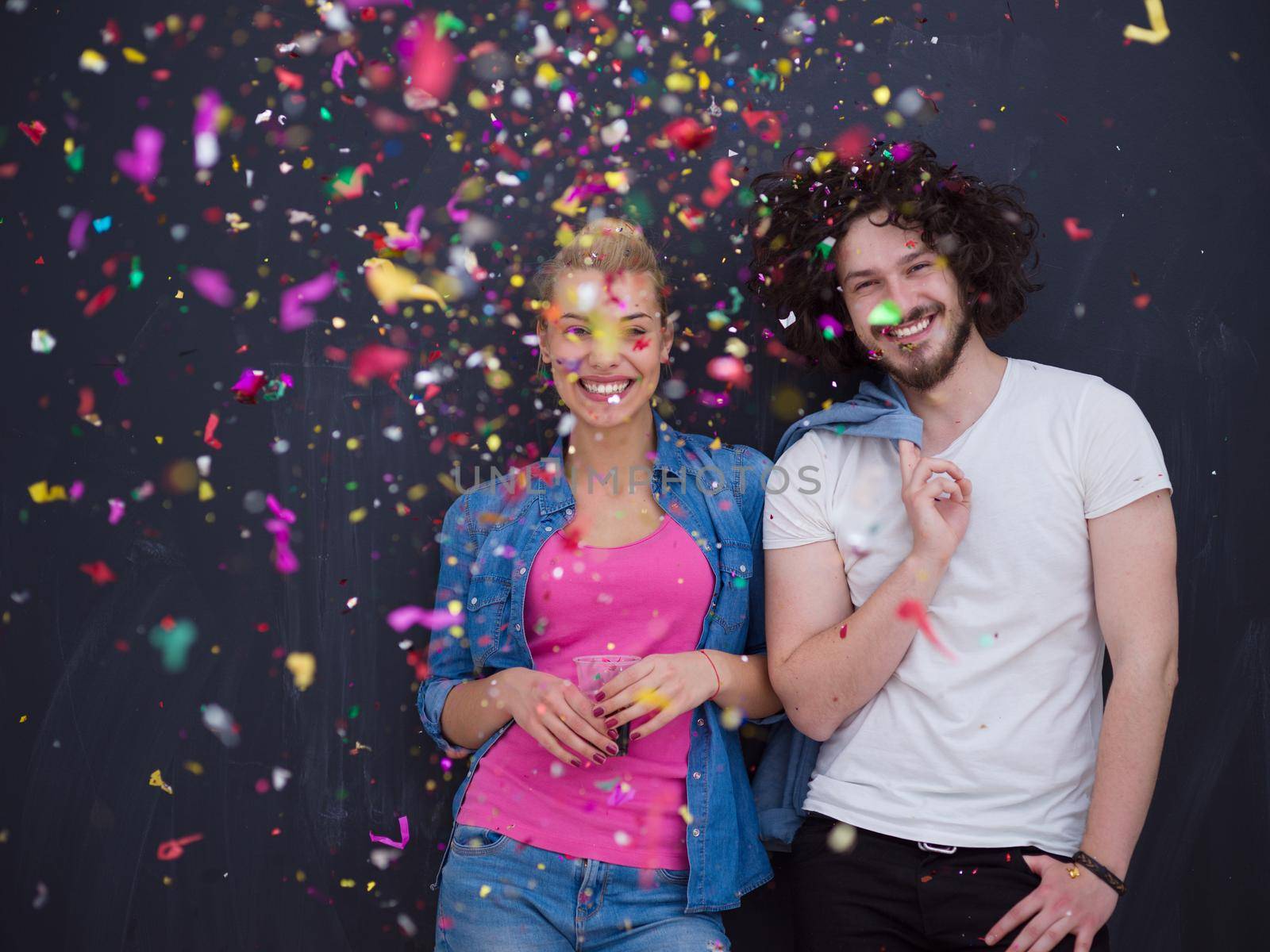 handsome young couple celebrating new year and chrismas party while blowing confetti decorations to camera isolated over gray background