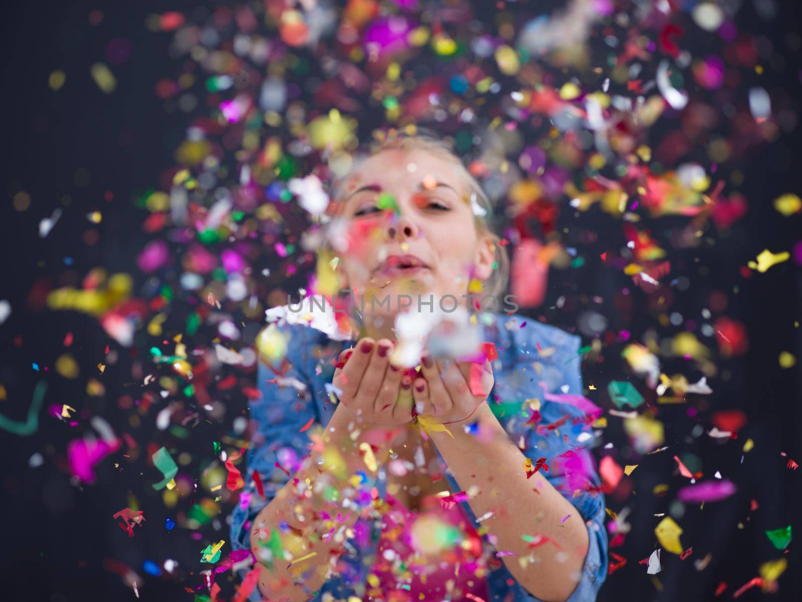 beautiful young woman celebrating new year and chrismas party while blowing confetti decorations to camera isolated over gray background