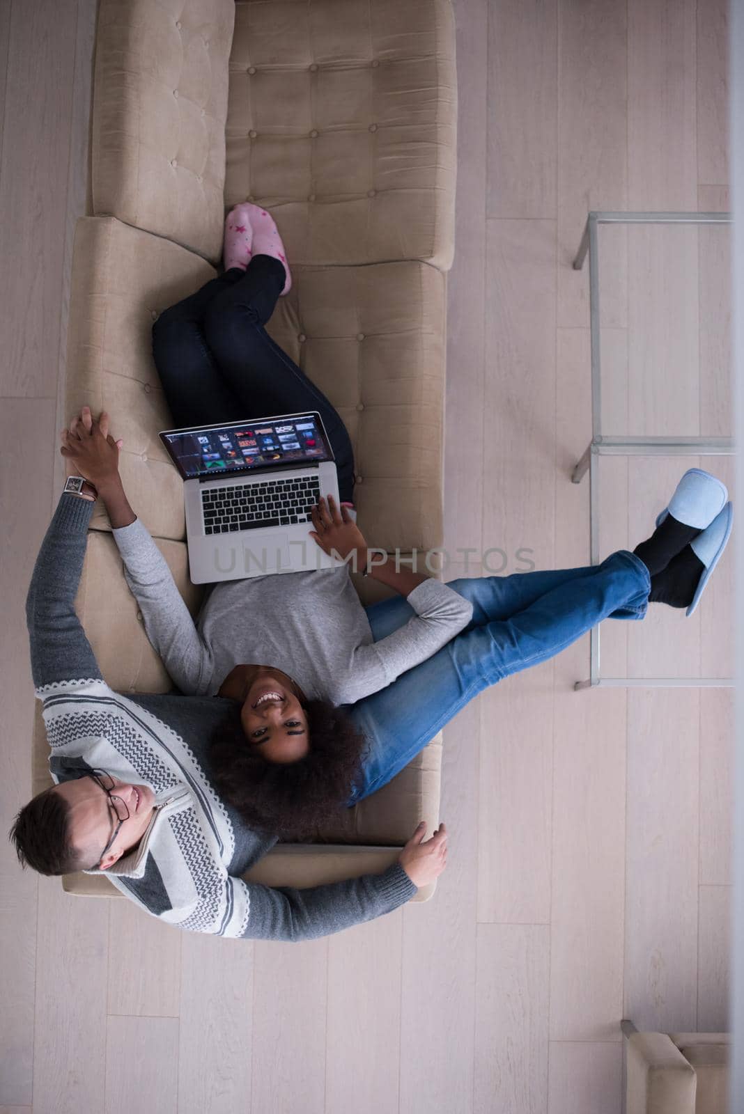 Young multiethnic couple relaxes in the luxury living room, using a laptop computer top view