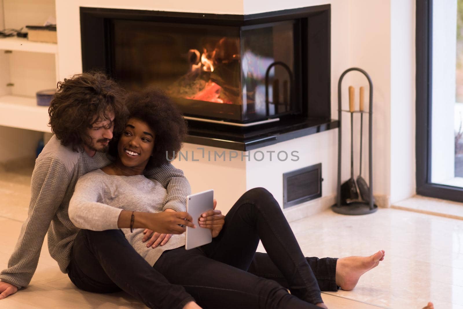 beautiful young multiethnic couple using tablet computer on the floor of their luxury home in front of fireplace at autumn day