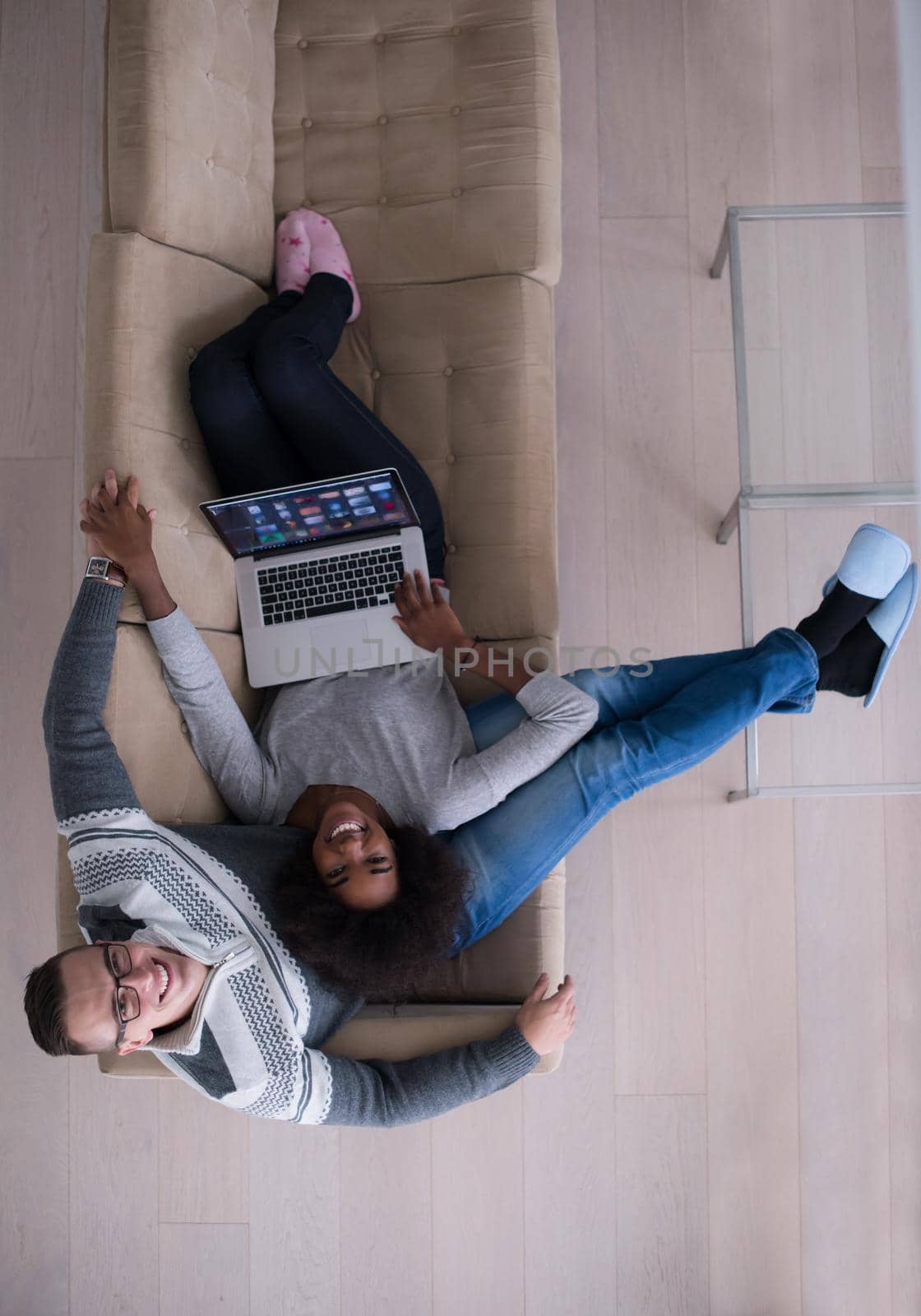 Young multiethnic couple relaxes in the luxury living room, using a laptop computer top view