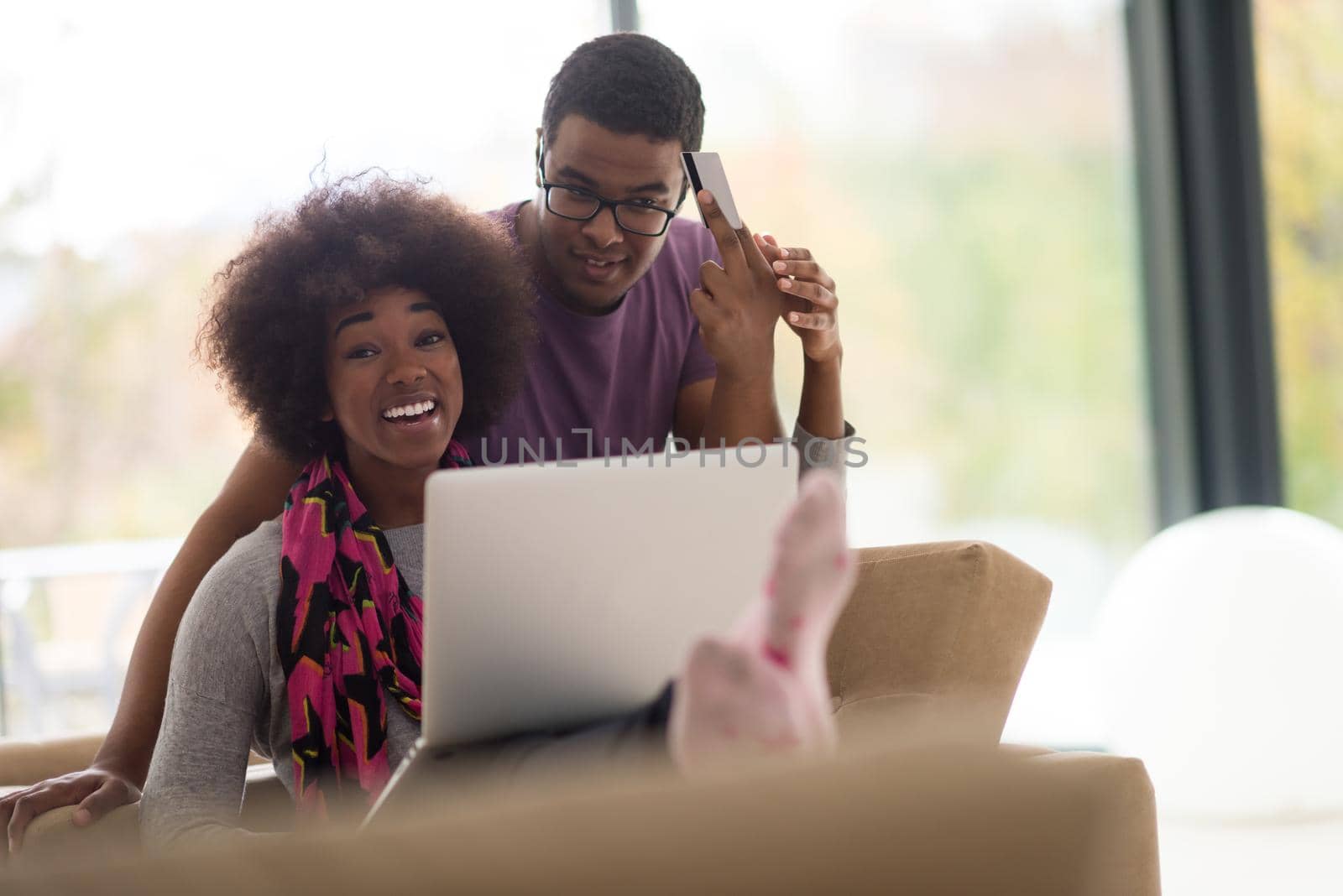 Happy young african american couple shopping online through laptop using credit card at home