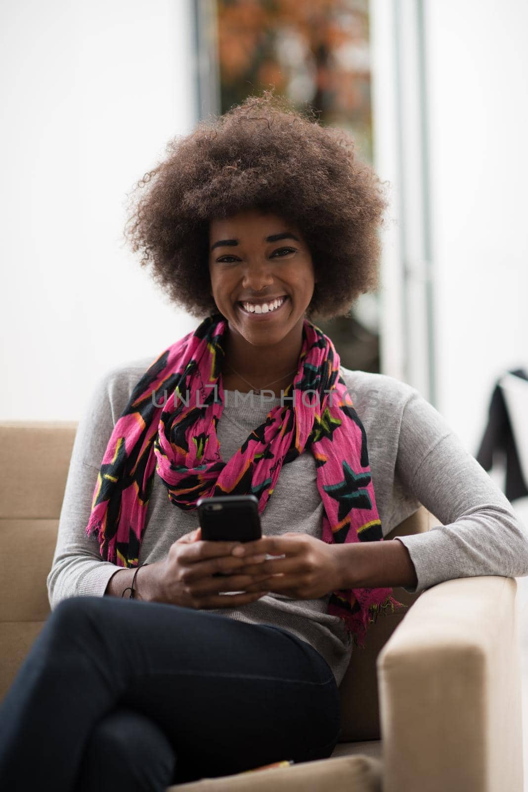 young happy african american woman sitting on sofa and using mobile phone at luxury home